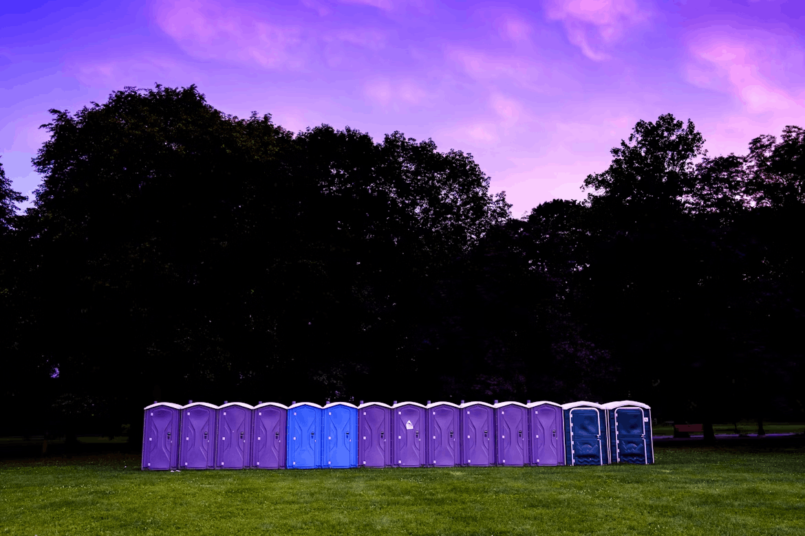 purple and blue porta potties lining a field at the edge of trees