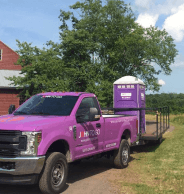 Toilet rental service truck in New York and purple porta potty