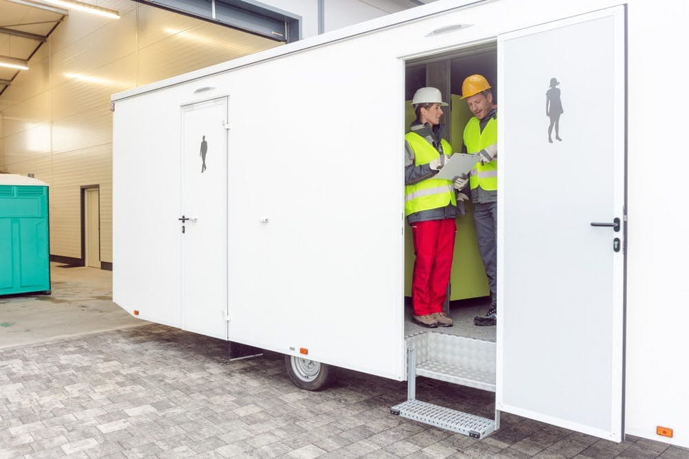 two workers looking at a clipboard inside a restroom trailer